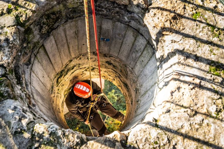 Technicien cordiste en descente sur corde dans un puits en béton, formation travaux en hauteur et espaces confinés